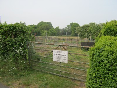 a rusted steel fence with a sign on it and allotments behind it.